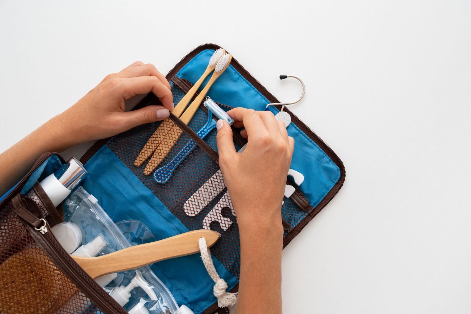 Hands packing a toiletry kit with toothbrush, soap dispenser, and containers in a blue zippered organizer
