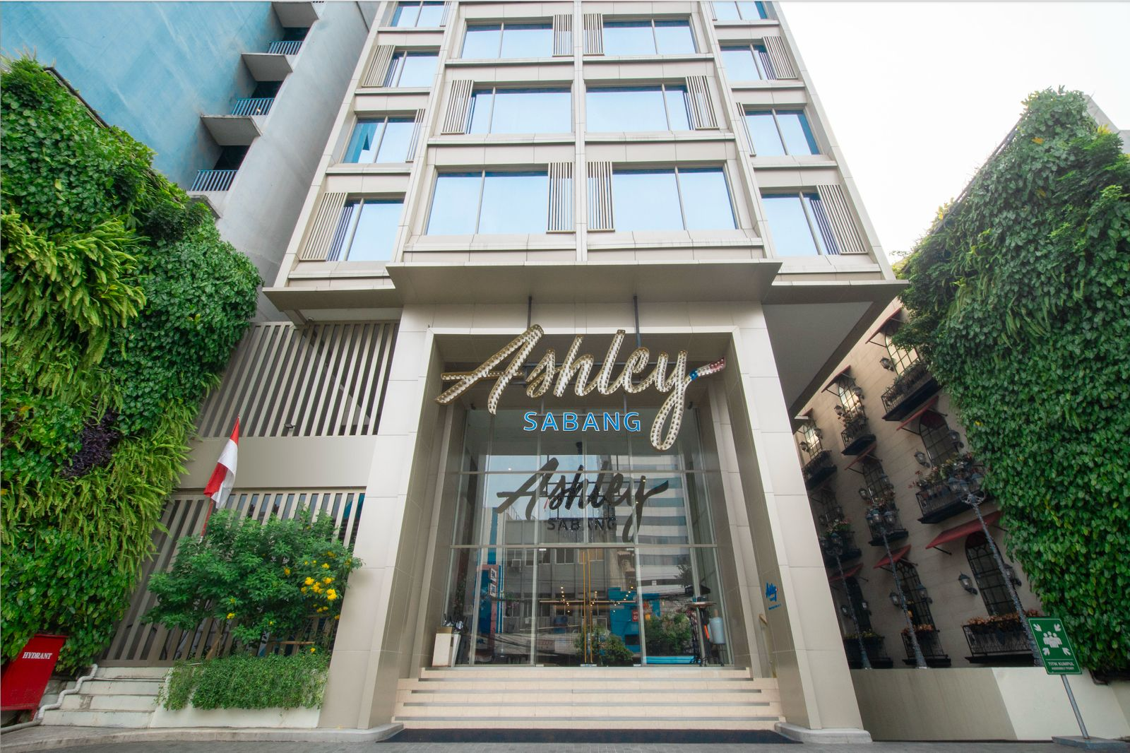 Infinity Hotel Sabang building facade with illuminated sign and glass entrance, framed by green hedges