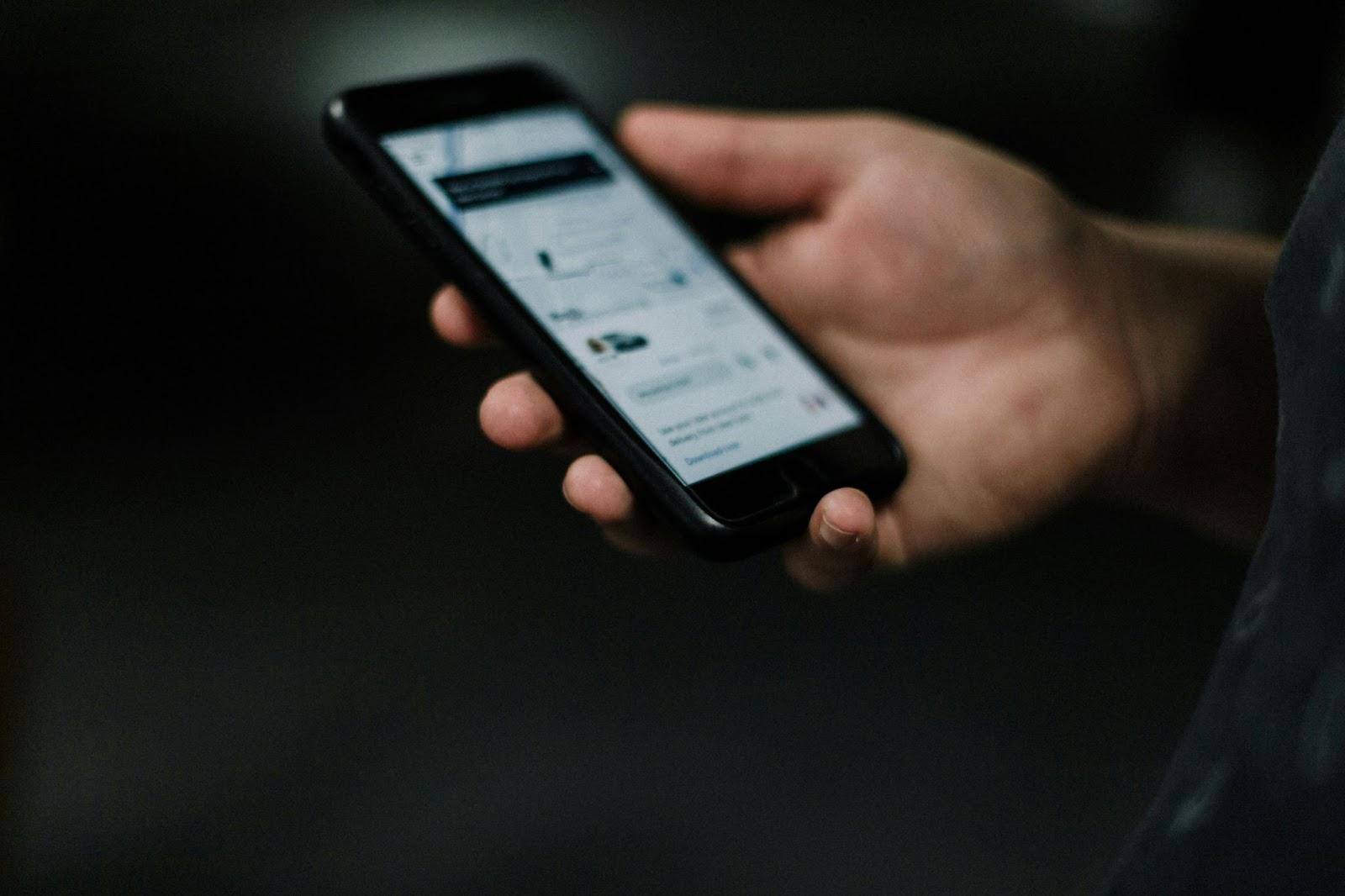 Person holding a smartphone displaying a social media feed with blurred background