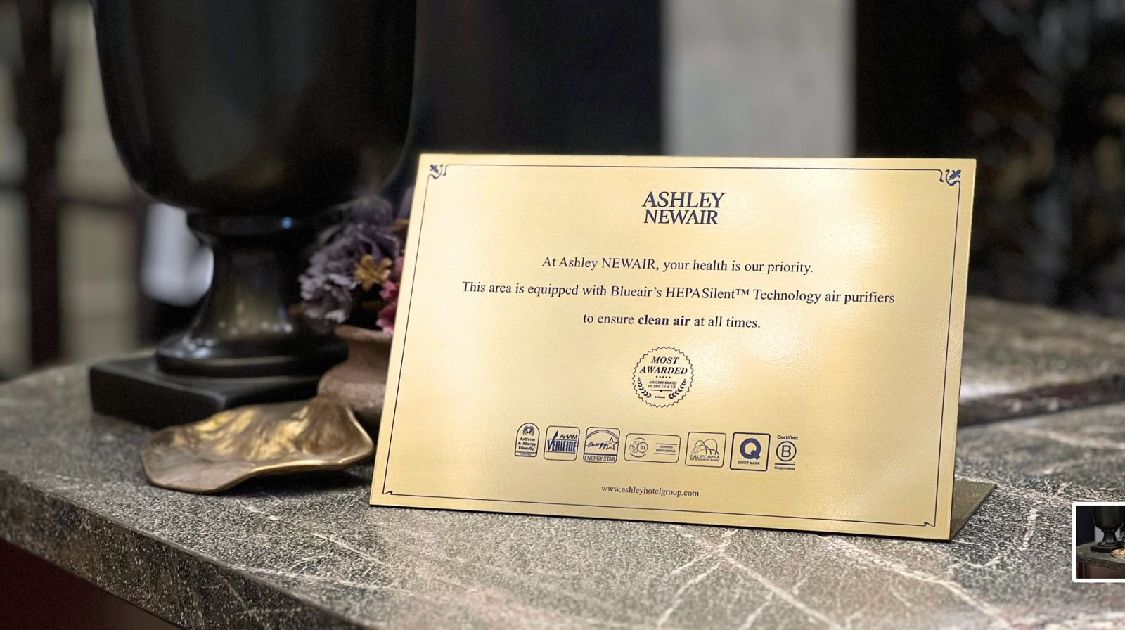 Ashley NEwAIR placard on hotel nightstand, featuring HEPA Silent technology and energy-efficiency certification icons