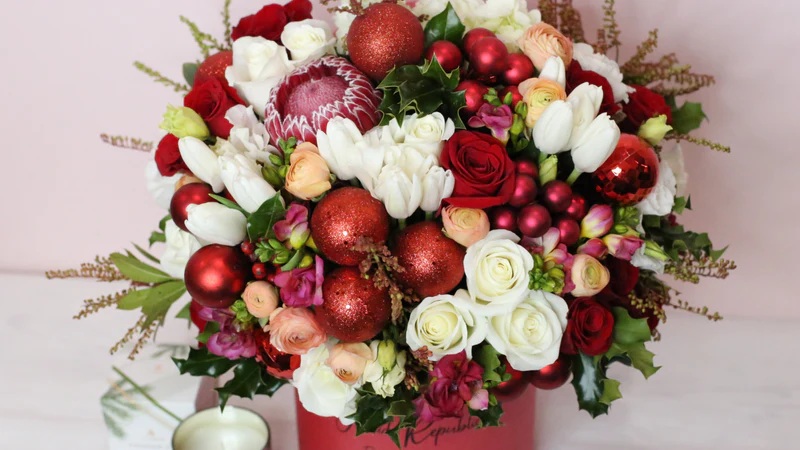 Festive red and white wedding bouquet with roses, tulips, glitter berries, and greenery on white background