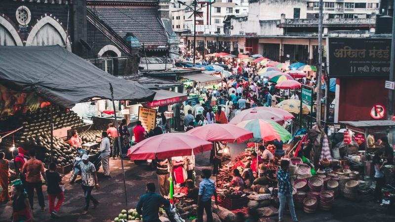 bustling street market with colorful umbrellas, stalls, and shoppers in a narrow urban lane