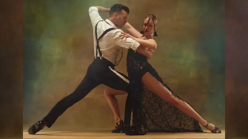 Couple dancing ballroom tango, man holding partner in flowing dress on a wooden floor