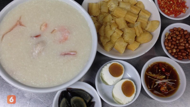 Ingredients for mixed rice porridge: bowl of pale rice soup with diced plantain, beans, chili sauce, and boiled eggs