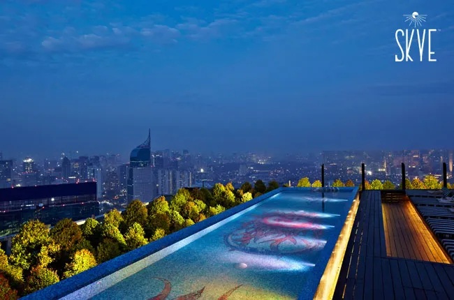 Skyline rooftop swimming pool at dusk with blue city lights and SKYE branding logo