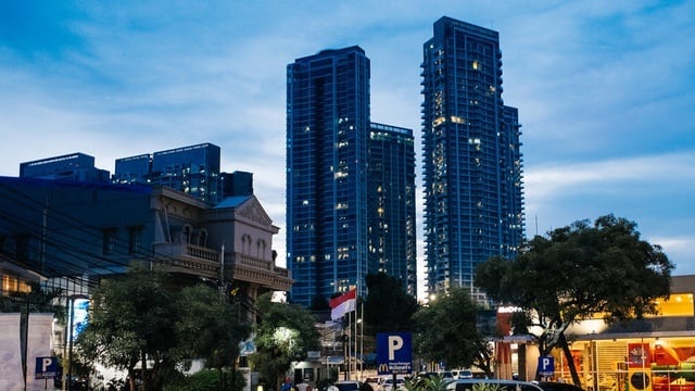 Downtown city skyline with tall blue skyscrapers at dusk, street traffic and trees in the foreground
