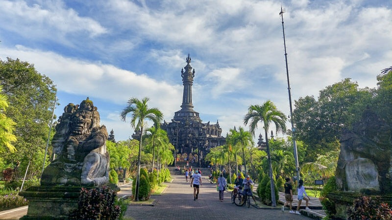 Prambanan temple complex in Bali with tall spire, palm trees, and visitors walking along the pathway