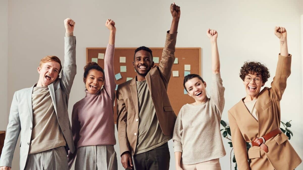 Diverse group of people cheering with raised fists in office, smiling and celebrating teamwork