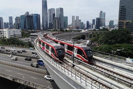 Red and white commuter trains on elevated tracks with skyline buildings in the background, urban transit hub