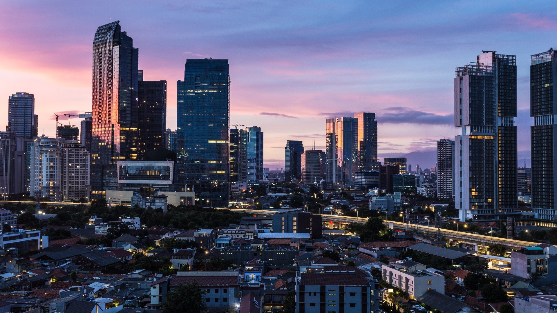 Downtown skyline with tall office towers at dusk, city lights glowing beneath pink-blue sunset sky
