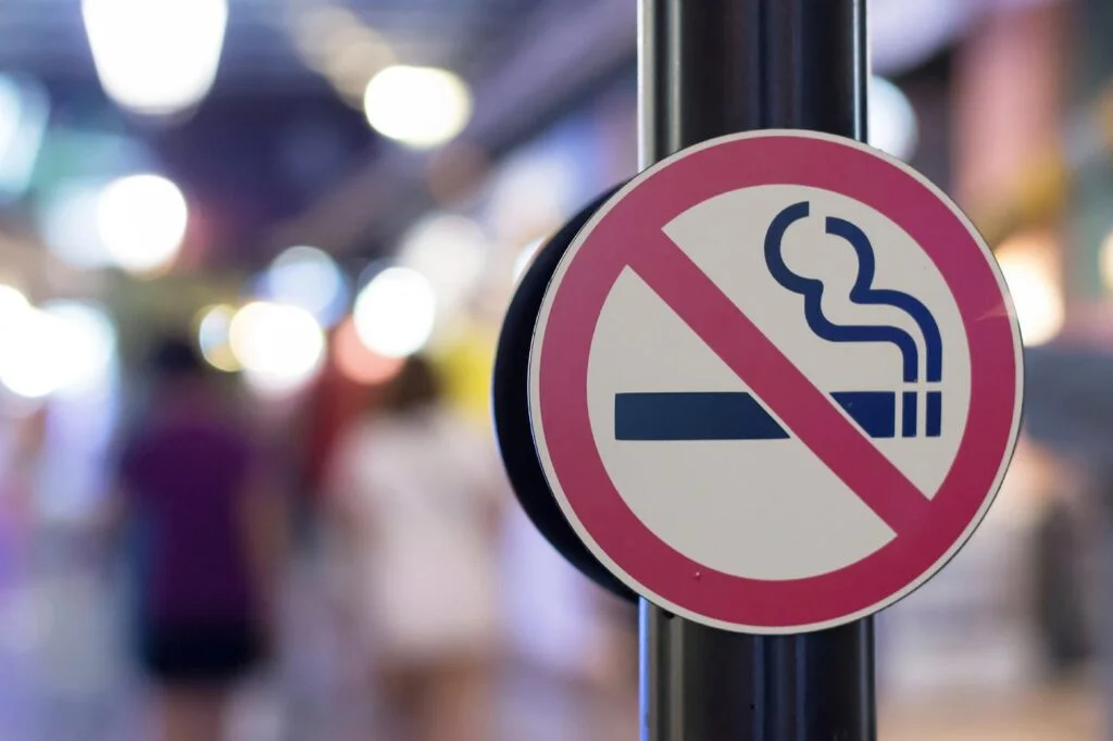 Smoking area prohibition sign with crossed-out cigarette icon on a street pole, blurred city background