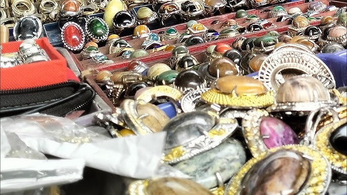 Close-up of mixed vintage jewelry rings and bracelets piled in a market stall, with a wallet in the foreground