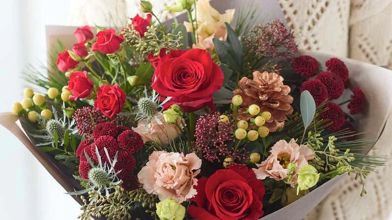Colorful mixed flower bouquet with red roses, pink carnations, and greenery arranged in wrapping paper