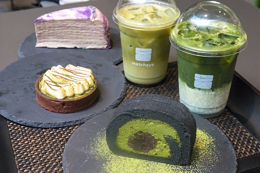 Matcha desserts on slate plates: green tea roll cake, matchaya mousse, and bottled matcha drinks on tray
