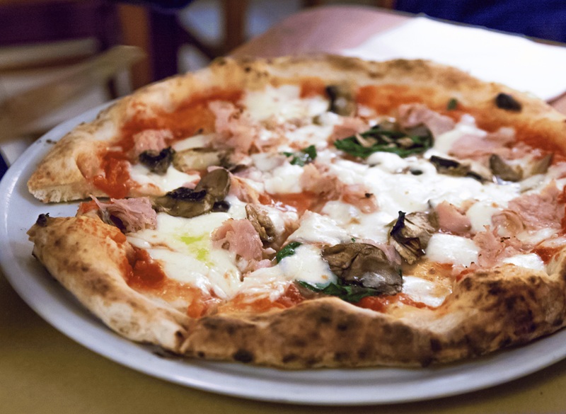 Neapolitan pizza with tomato sauce, mozzarella, ham, mushrooms, and fresh herbs on a white plate