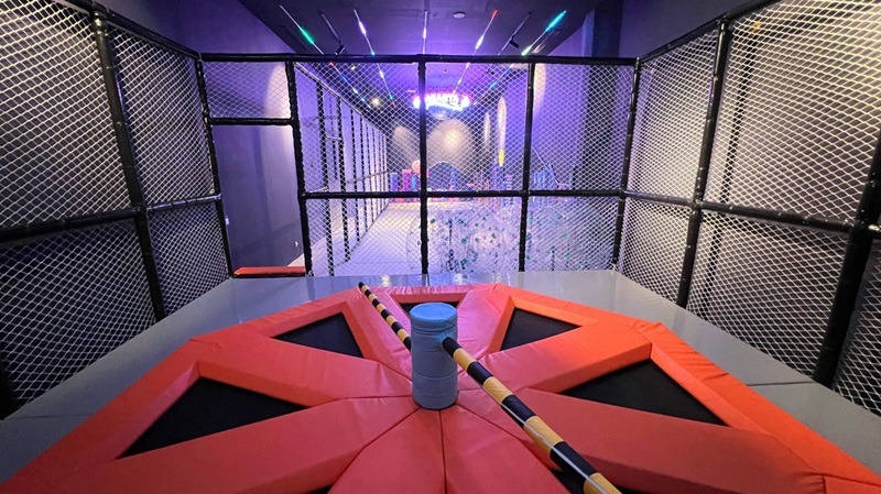 Trampoline park arena with orange padded barriers and black netted walls surrounding a bounce area