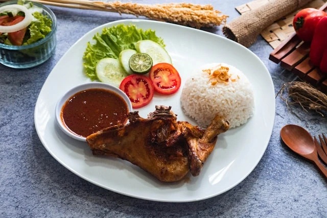 Plate of grilled chicken, steamed rice, tomato and cucumber salad with dipping sauce, meal presentation on table