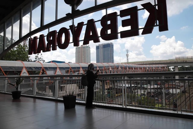 Man standing on rooftop terrace with railing and city skyline behind, large rust-colored “TOMORROW” sign overhead