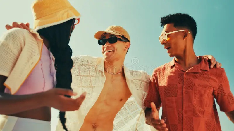 Group of friends laughing outdoors wearing hats and sunglasses, close-up conversation in warm sunlight
