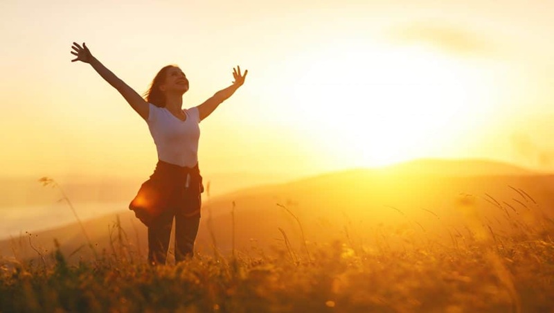 Woman running through golden wheat field at sunset with arms outstretched
