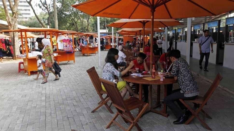Street food market with people dining under orange canopies, stalls and shoppers along a paved walkway