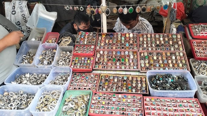rows of colorful rings and pendants displayed in trays at a jewelry market stall