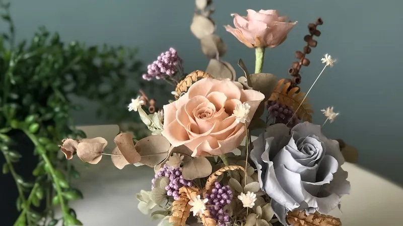 Bouquet arrangement with peach and gray roses, purple flowers, and eucalyptus leaves on a blurred background