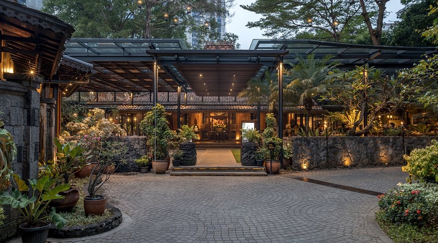 Lush courtyard with stone wall, potted plants, brick walkway, and warm outdoor lighting at night