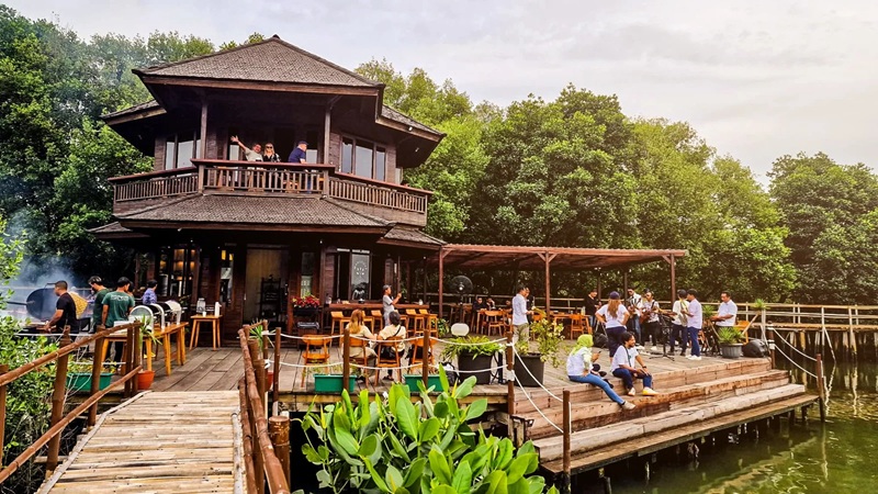 Outdoor floating restaurant with people dining by riverside wooden dock and stilt house near trees