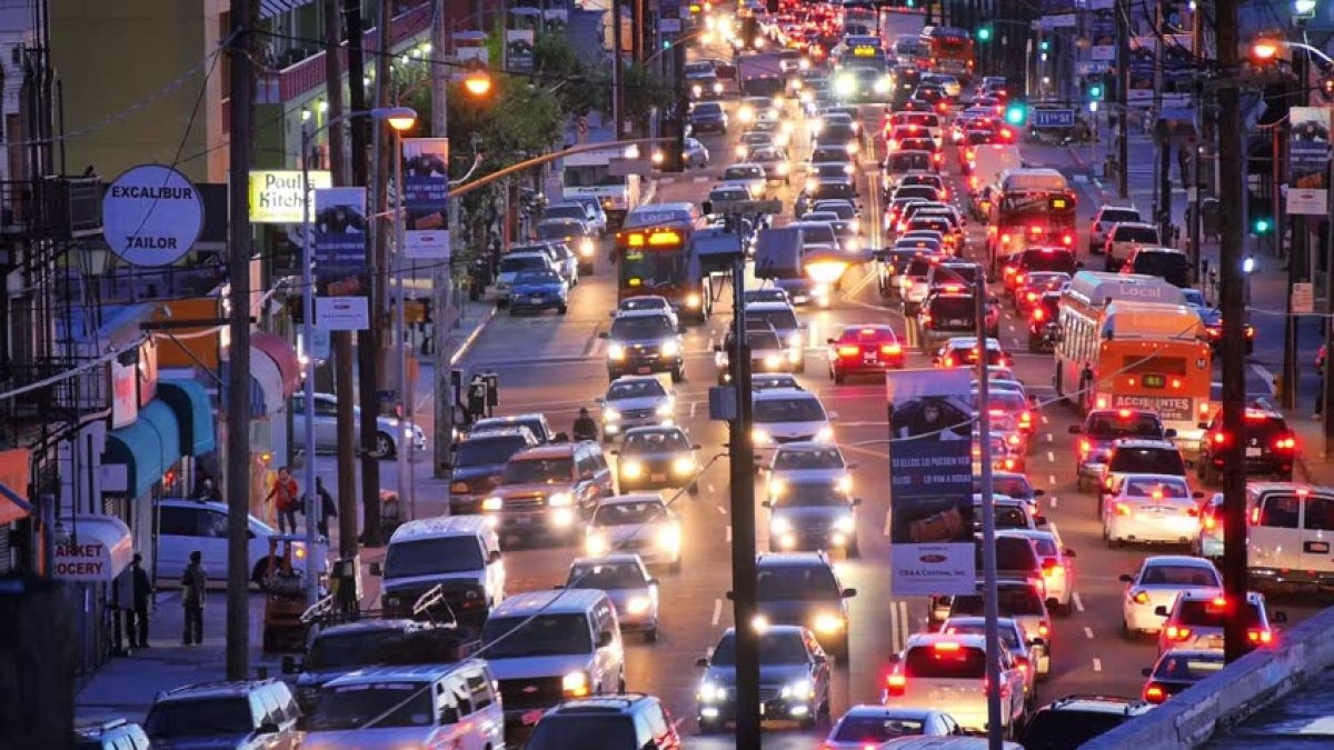 Busy city traffic with cars and buses lined up on a crowded street at dusk, glowing brake lights and headlights