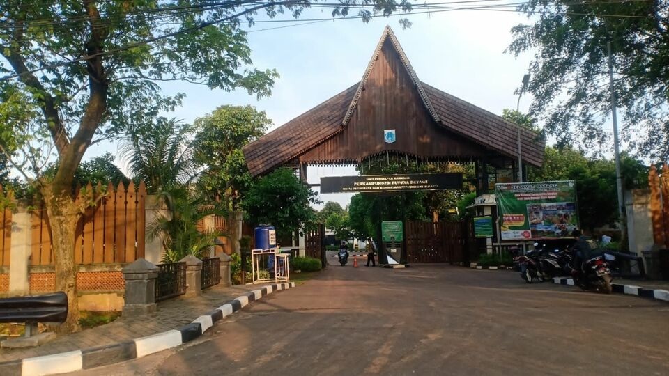 Taman rumah kayu joglo gerbang masuk dengan papan nama, deretan motor di halaman, dan pepohonan sekitar