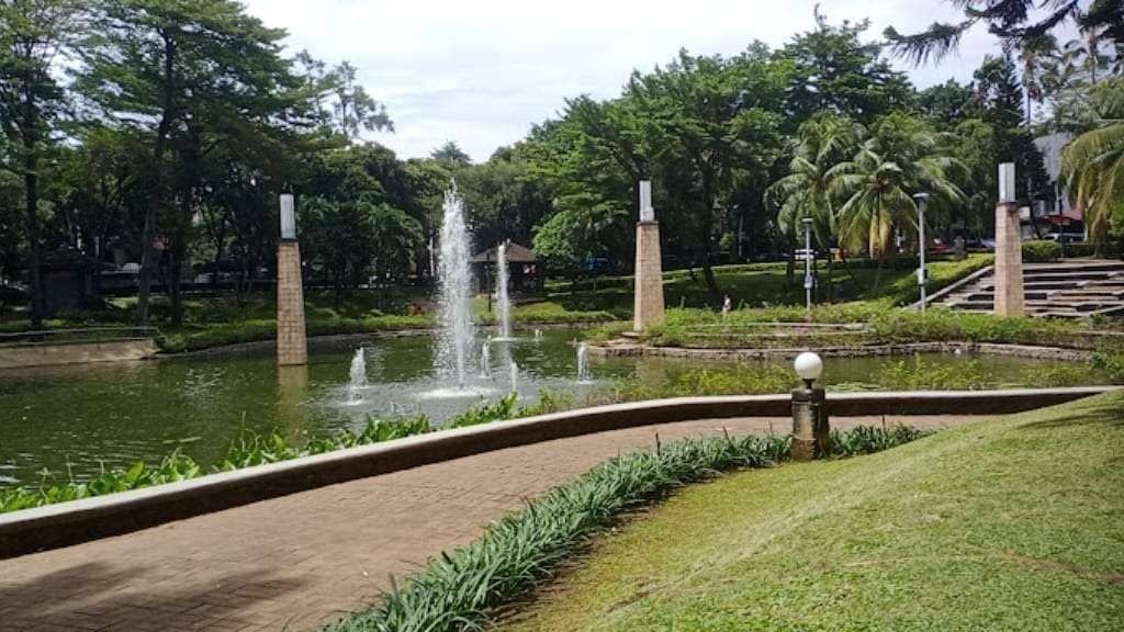 Lush garden pond with fountain jets, brick pillars, manicured lawn, and palm trees in daylight
