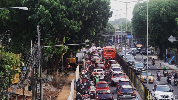 Heavy traffic on urban road with cars, motorcycles, and construction lanes beside green trees and streetlights