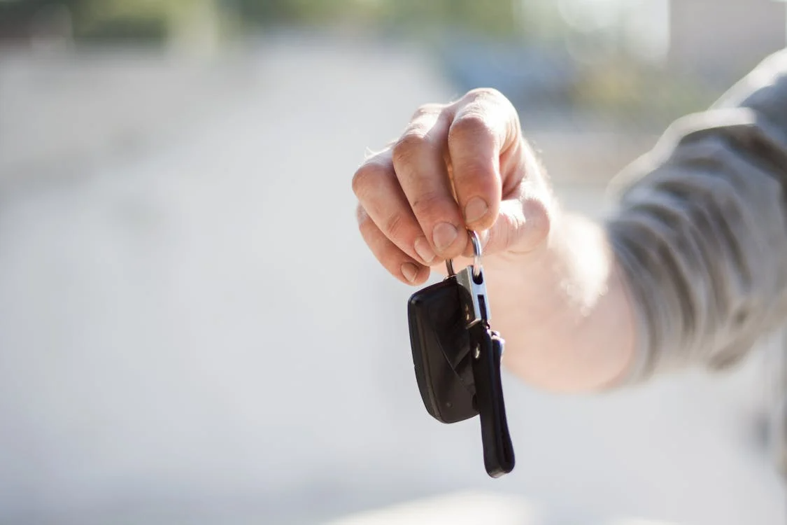 Person holding car keys in hand, handing over vehicle key fob outdoors