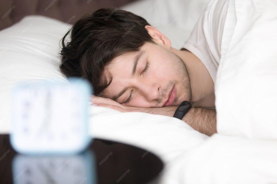 Man sleeping in bed wearing smartwatch, resting peacefully while arm and pillow are in foreground