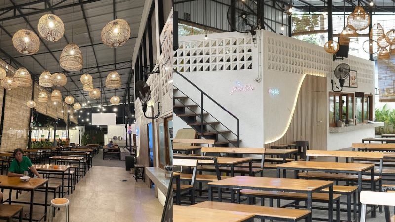 Spacious restaurant interior with wooden tables, ceiling pendant lights, and white wall with staircase and decor
