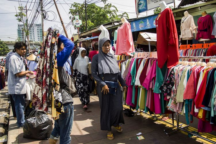 Outdoor clothing market stall with colorful shirts and dresses, shoppers walking between racks under sunlight