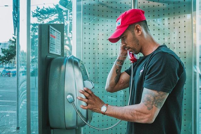 Man in red bucket hat and green shirt using a charging station outdoor, plugging cable into a device