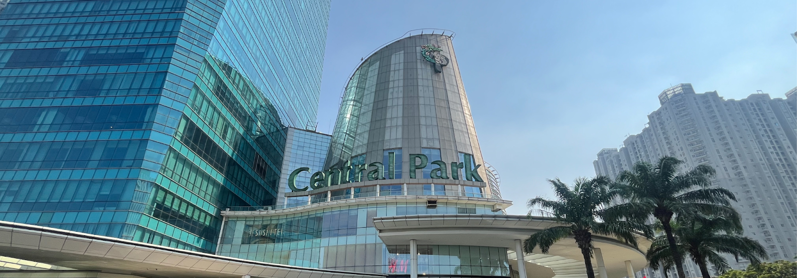 Central Park building with green “Central Park” sign, modern glass towers, palm trees, and clear sky