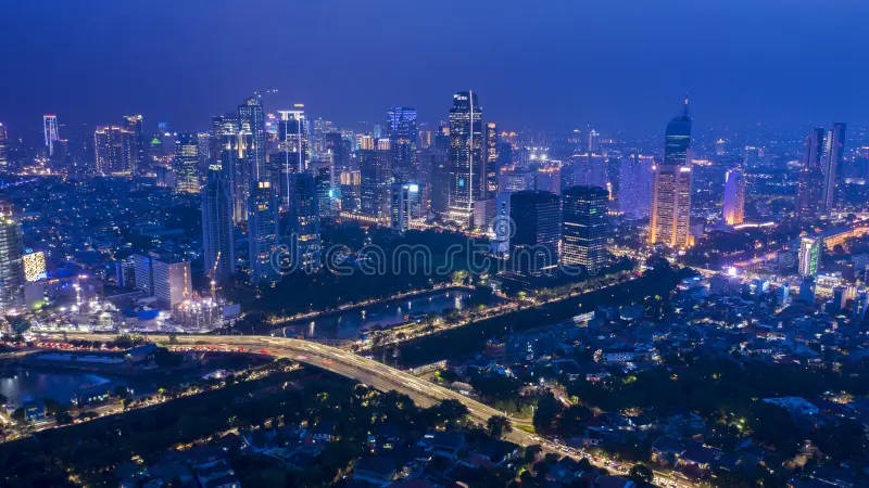Night aerial view of a modern city skyline with a river and illuminated bridges in the background
