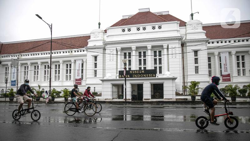 Museum Bank Indonesia building with red-tiled roof, pedestrians on bikes, and rain-wet street in front