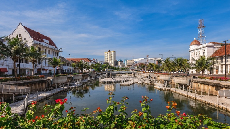 Canal with palm trees, colonial buildings, and a tall clocktower by the water under a blue sky