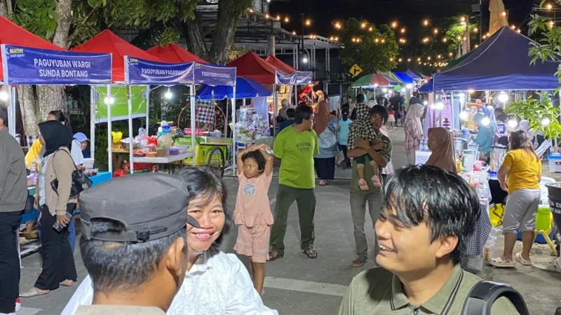 Night market scene with colorful food stalls and string lights, people walking and chatting at outdoor venue