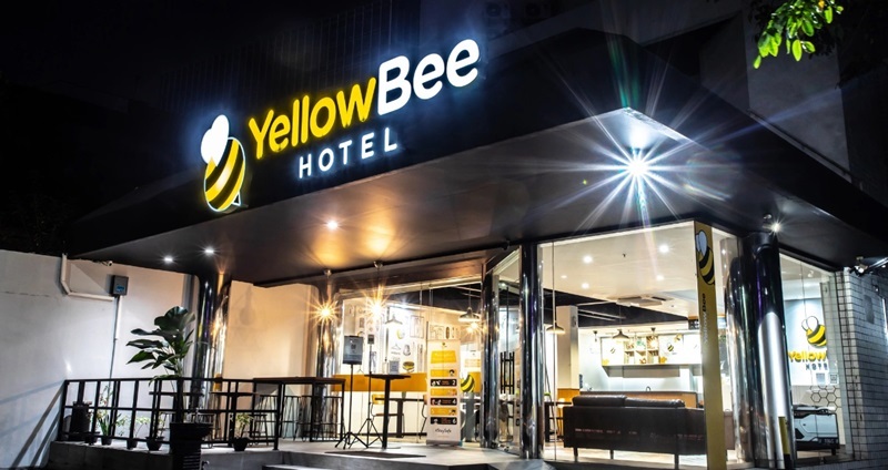 YellowBee Hotel entrance at night with illuminated sign, glass doors, and bright exterior lights