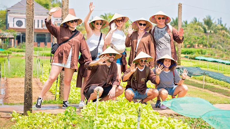 Group of kids wearing sun hats and waving while kneeling in a garden with raised beds outdoors