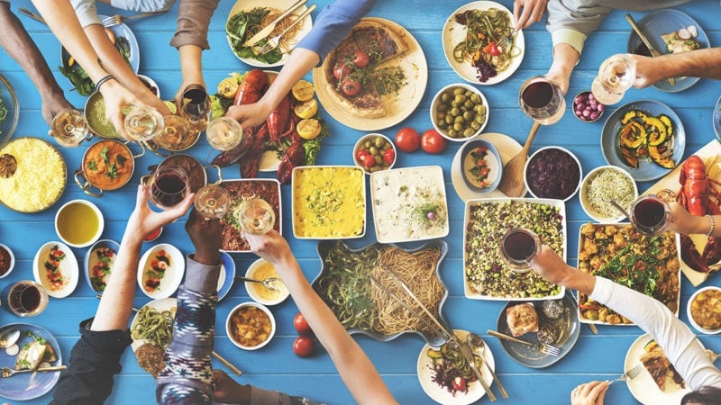 Group meal with friends serving and sharing bowls and plates of Mediterranean food on a blue tablecloth