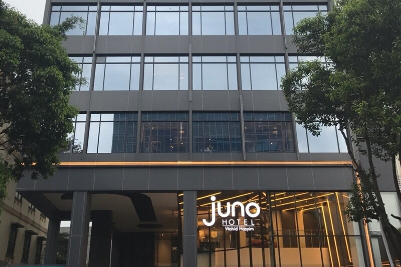 Juno Hotel entrance sign above glass-front building with trees framing the facade
