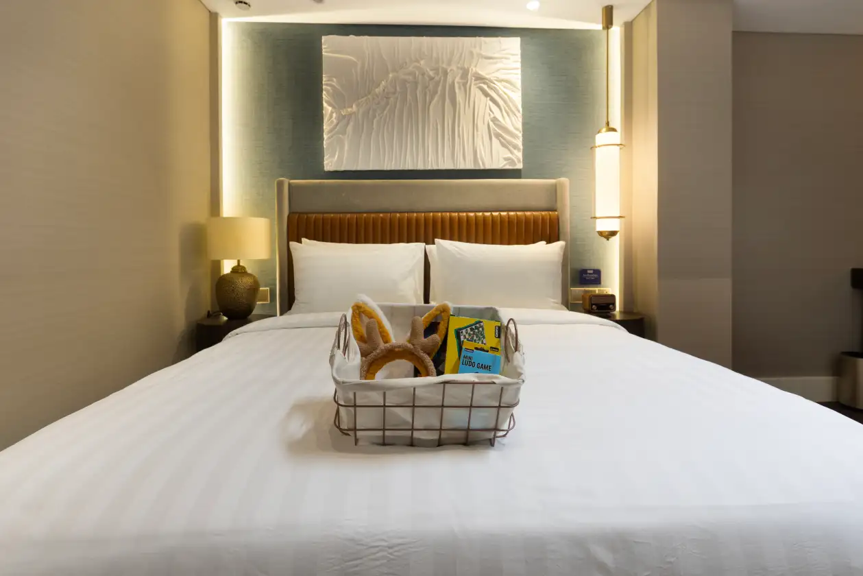 Modern hotel bedroom with neatly made bed, two pillows, and welcome basket on the mattress