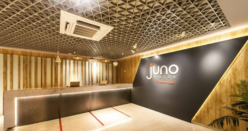Modern hotel lobby reception area with illuminated LED wall, Juno Hotel logo, and wood paneling ceiling