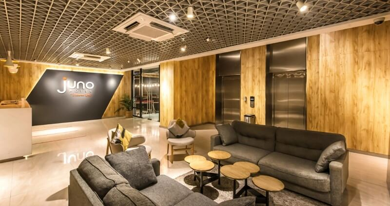 Modern office lounge with wooden walls, sofas, coffee tables, and elevators in the background